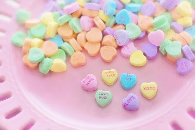 Sur fond roses, un tas de bonbons en forme de coeurs et de couleurs pastelles portant des messages d'amour.