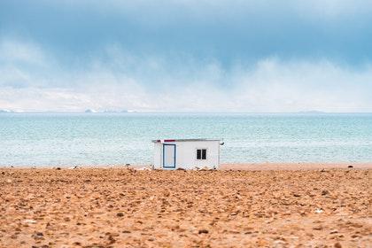 Sur une plage avec une mer très bleue on voit une cabane blanche.
