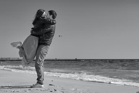Un homme porte une femme dans ses bras et ils s'embrassent sur la plage.