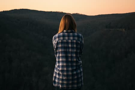 Une femme seule, de dos, face au coucher de soleil.