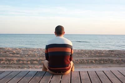 Un homme est assis seul au bord d'une plage, il regarde l'horizon.