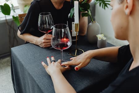 Une petite table avec deux verres de vin rouge tenus par un couple