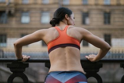 Vue de dos une femme en tenue de sport s'appuie sur une rembarde en ville.