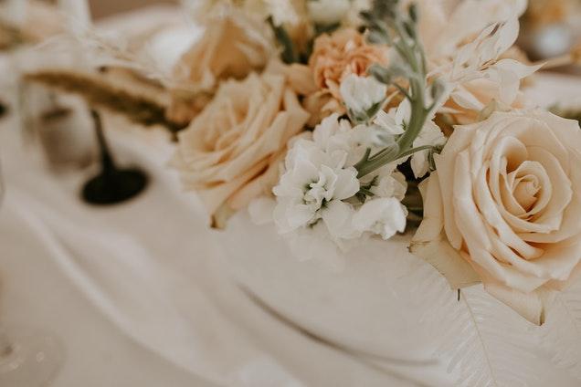 Sur une table blanche dressée on voit un bouquet de fleurs roses et blanches.