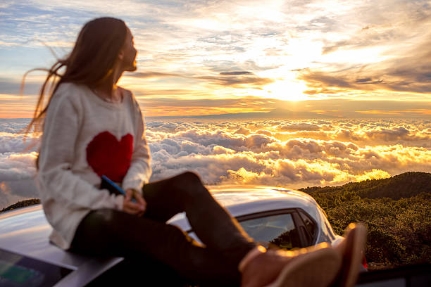 jeune femme portant un sweat avec un coeur regardant le coucher du soleil sur une voiture